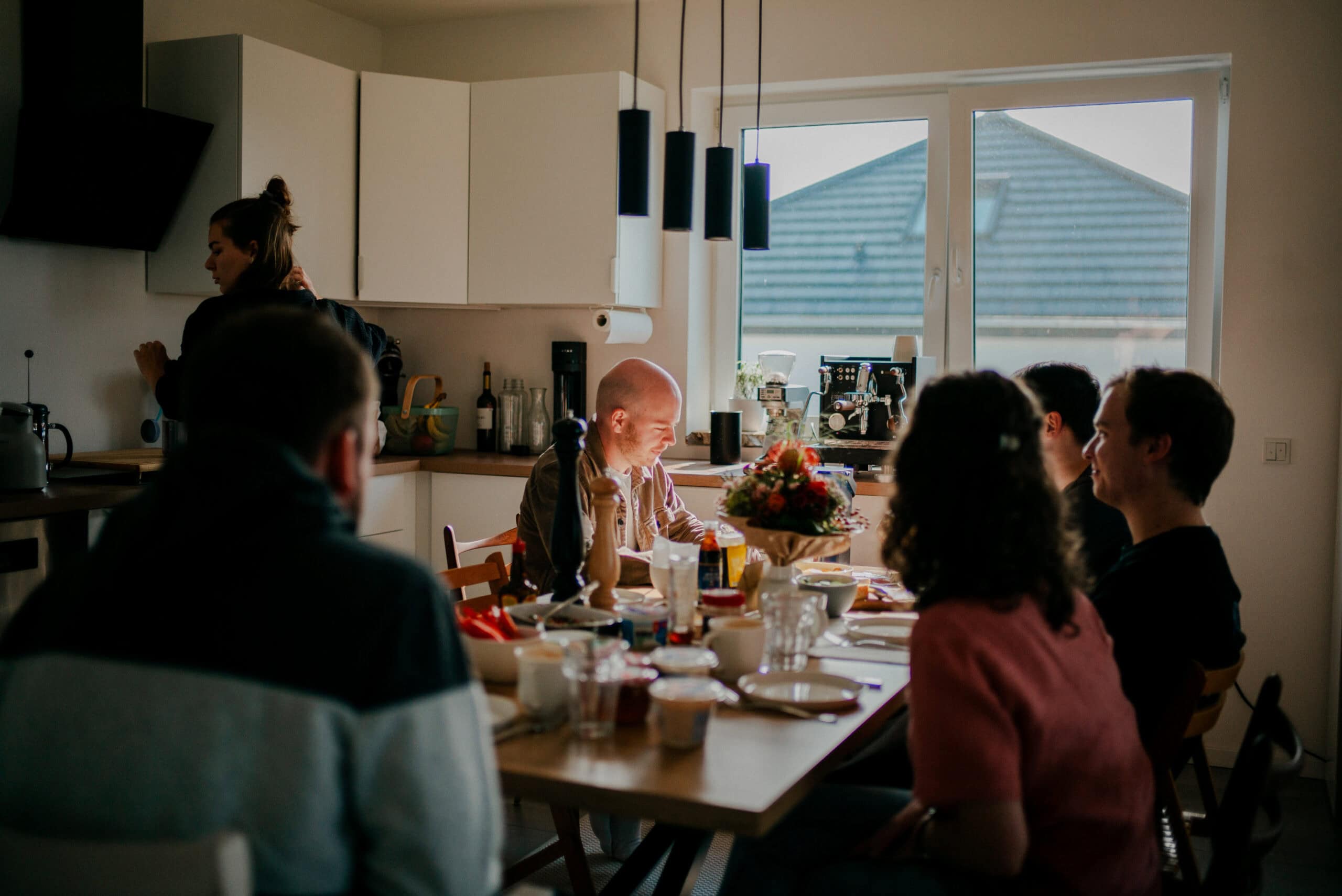 Geselliges Beisammensein beim Frühstück in einer modernen Küche, Familie oder Freunde genießen eine Mahlzeit, helles Tageslicht, gemütliche Atmosphäre, gemeinsames Essen, hausgemachte Speisen, Mosaikkirche Bitburg.